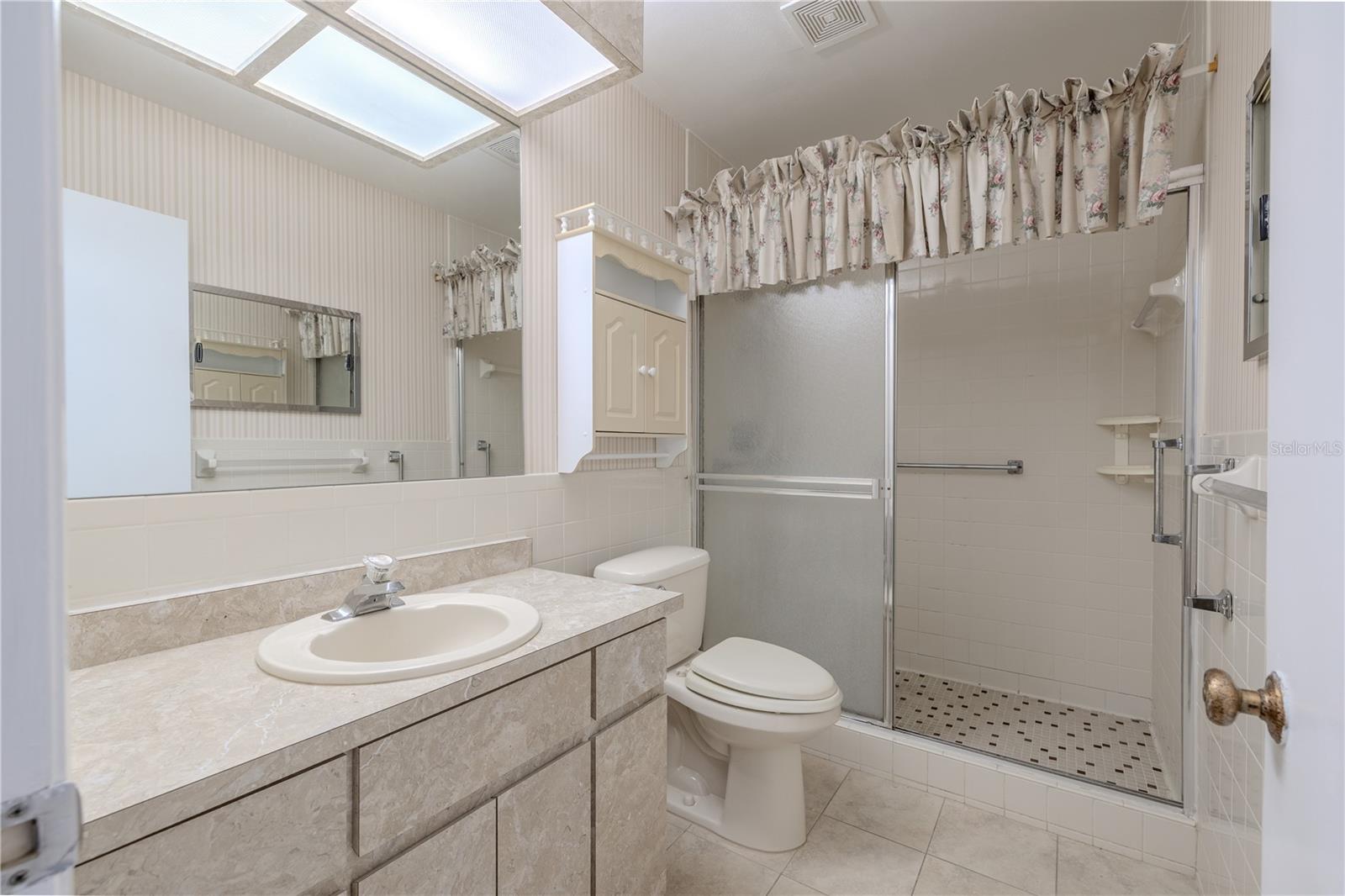 Primary bathroom features a  tile floor, a mirrored vanity with storage, and a step in shower with grab bar.
