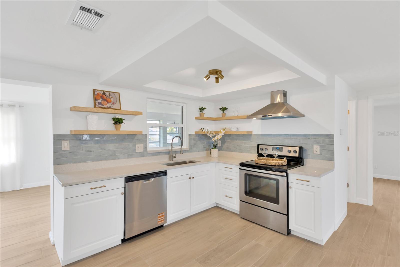 Enjoy open kitchen with a modern flair features subway tile backsplash, accent shelves, range hood, en-trend lighting and stainless appliances.