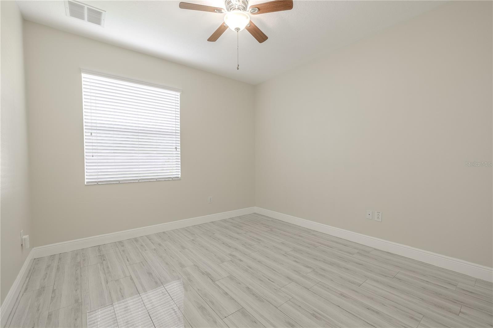 The (1st floor) 4th bedroom features porcelain plank tile flooring, neutral tone walls and a ceiling fan with light kit.