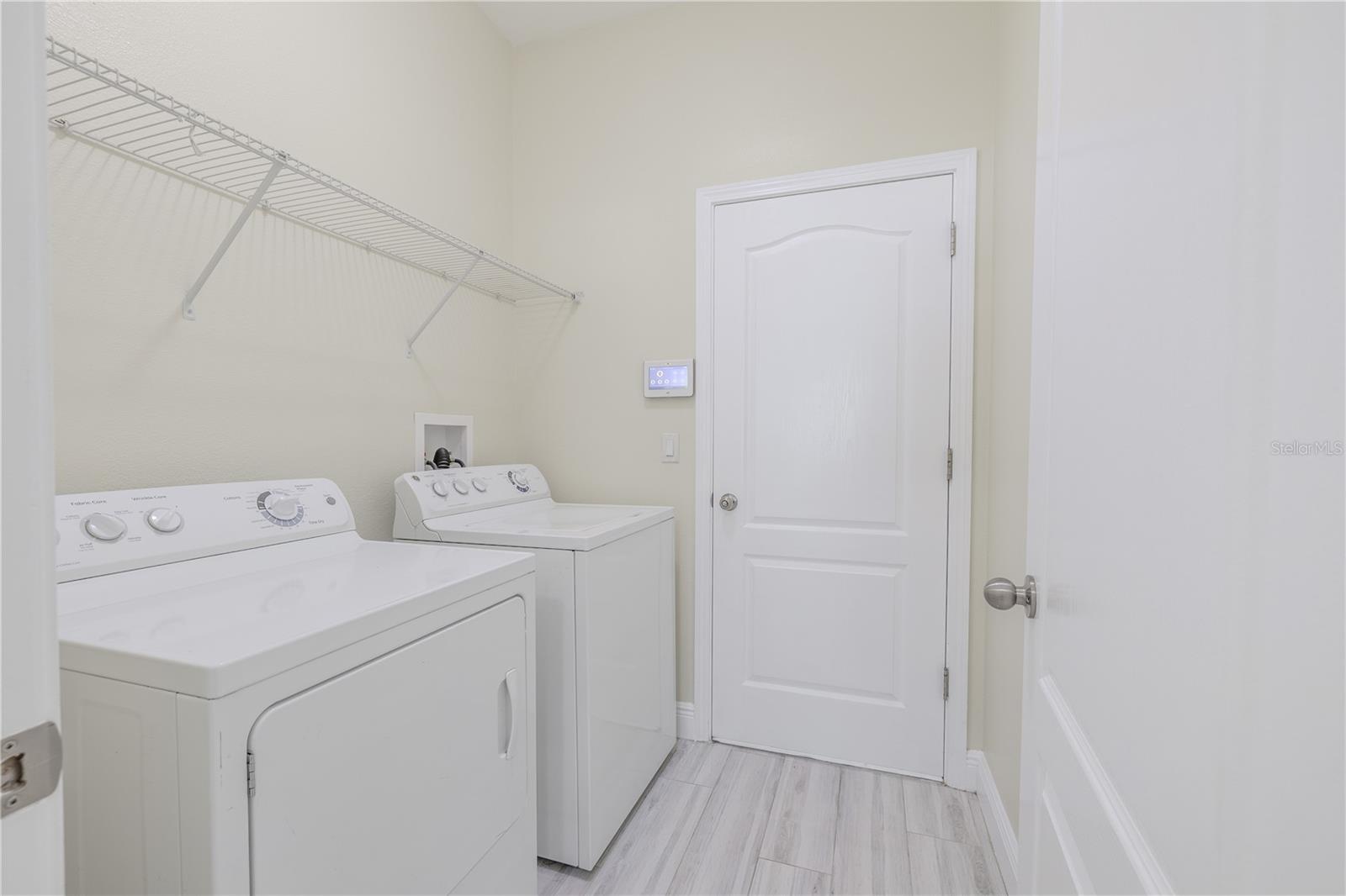The Laundry room has a  porcelain plank tile floor, GE washer & dryer, and shelving above.