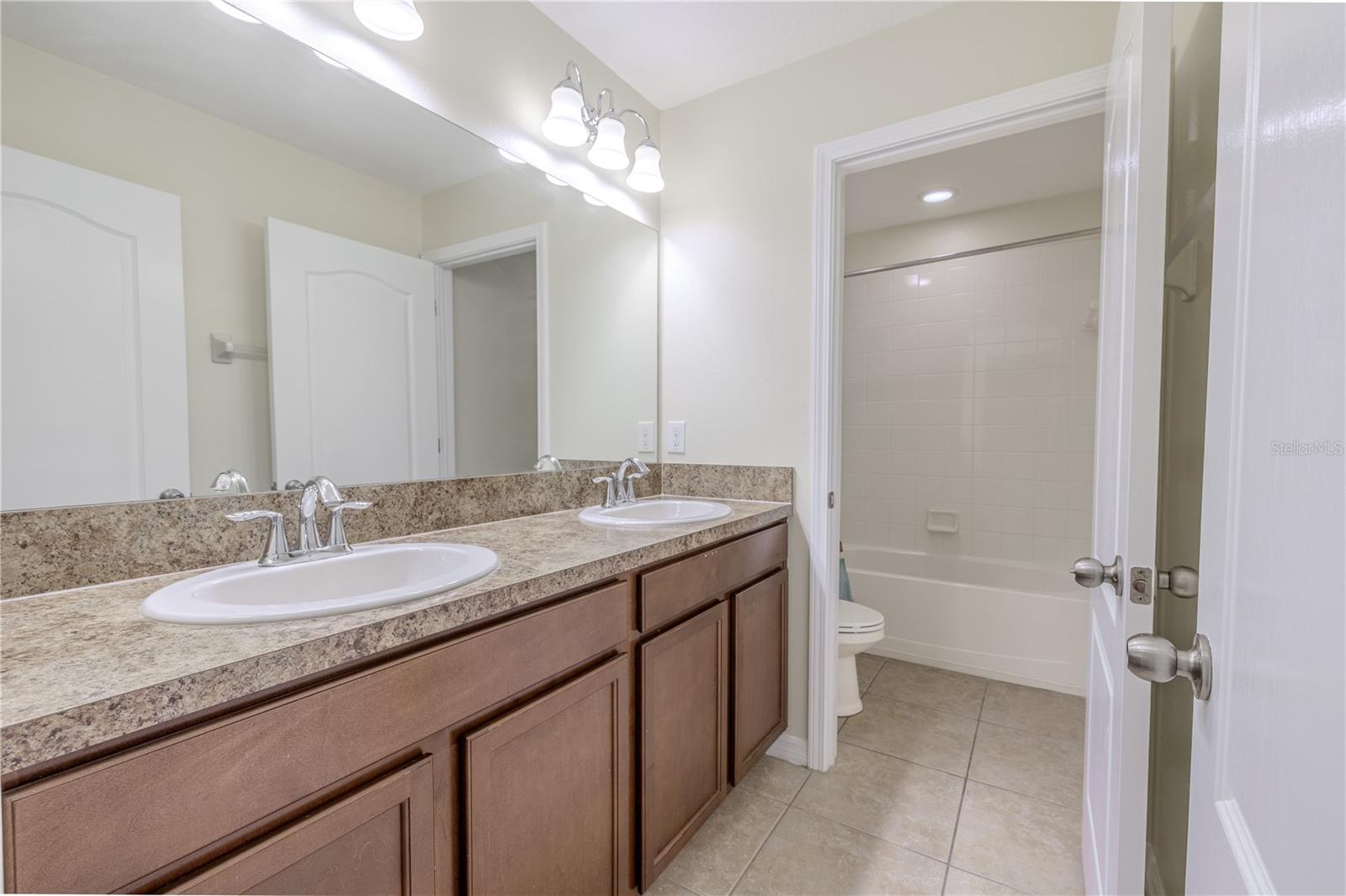 2nd bathroom features a dual sink, mirrored wood vanity with storage and granite counter top and a tub with shower.