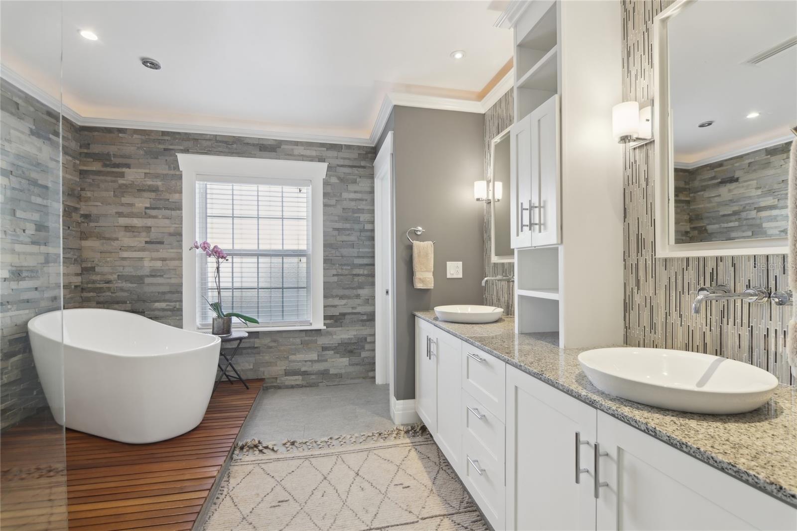 The primary bathroom features teak floor accents, a freestanding tub with a towel warmer, and a walk-in shower with rain head and body jets.
