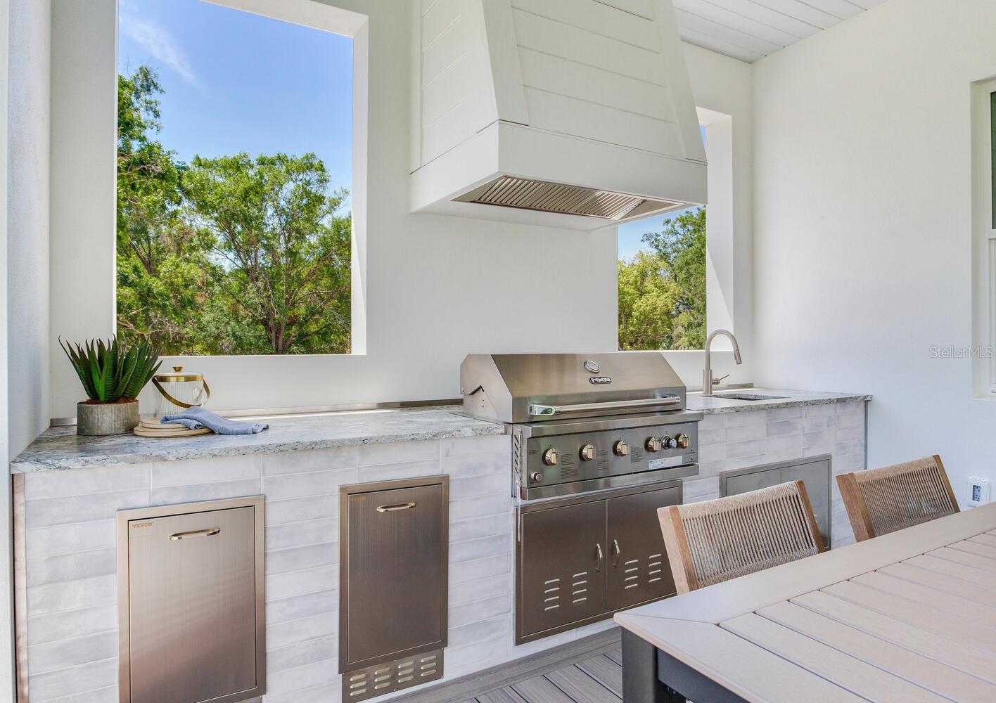 Outdoor kitchen with grill and hood area as well as a sink.  The entire kitchen is beautifully framed between two "windows"