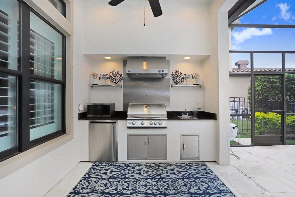 Outdoor summer kitchen with mini fridge, microwave, sink, grill, GE Monogram vented hood.