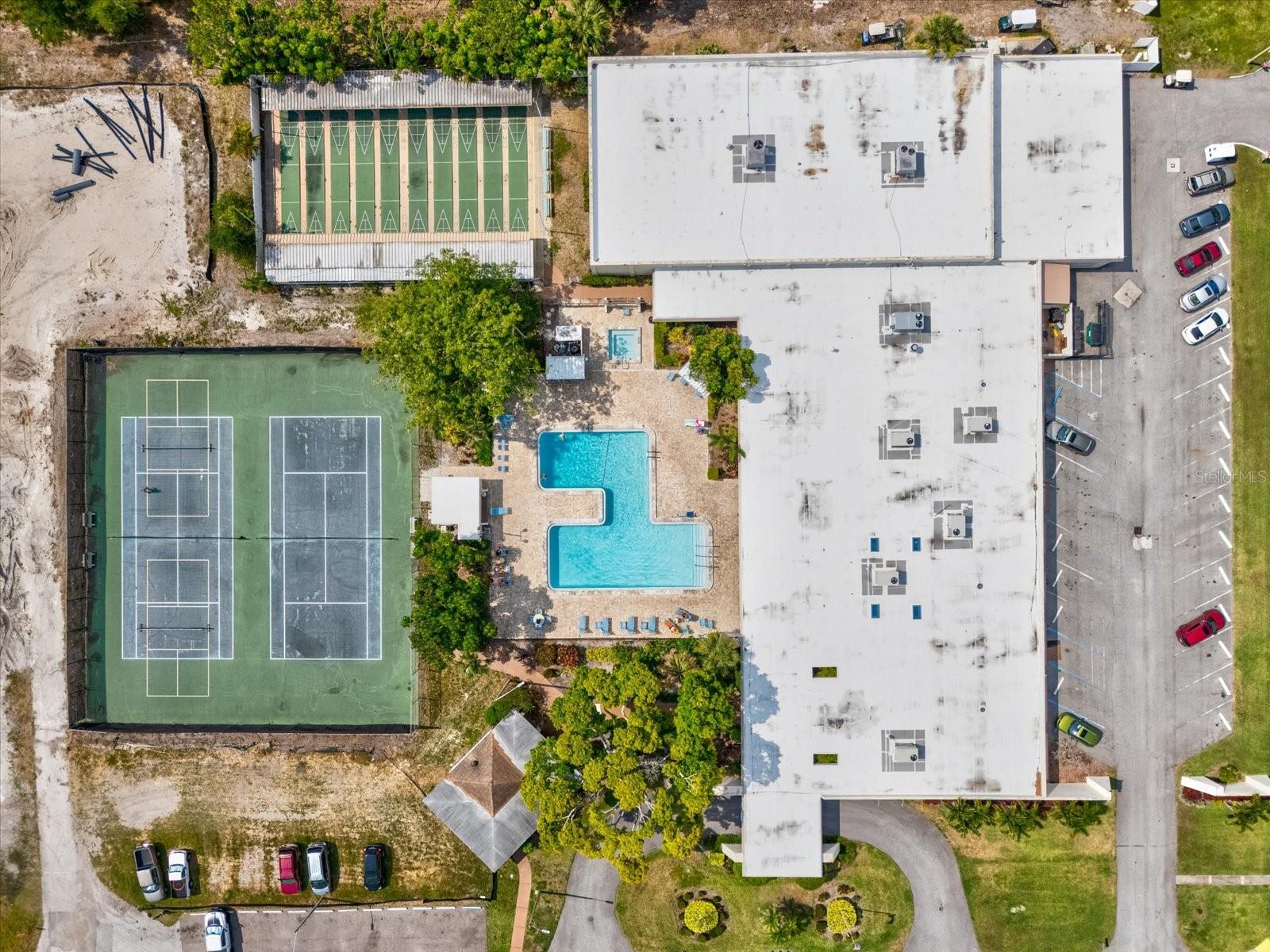 Overhead view of tennis, pickball and shuffleboard courts along with 1 of the 6 pools.  This is also an aerial of one of the Clubhouses located in the complex offering a wide variety of activities throughout the week.