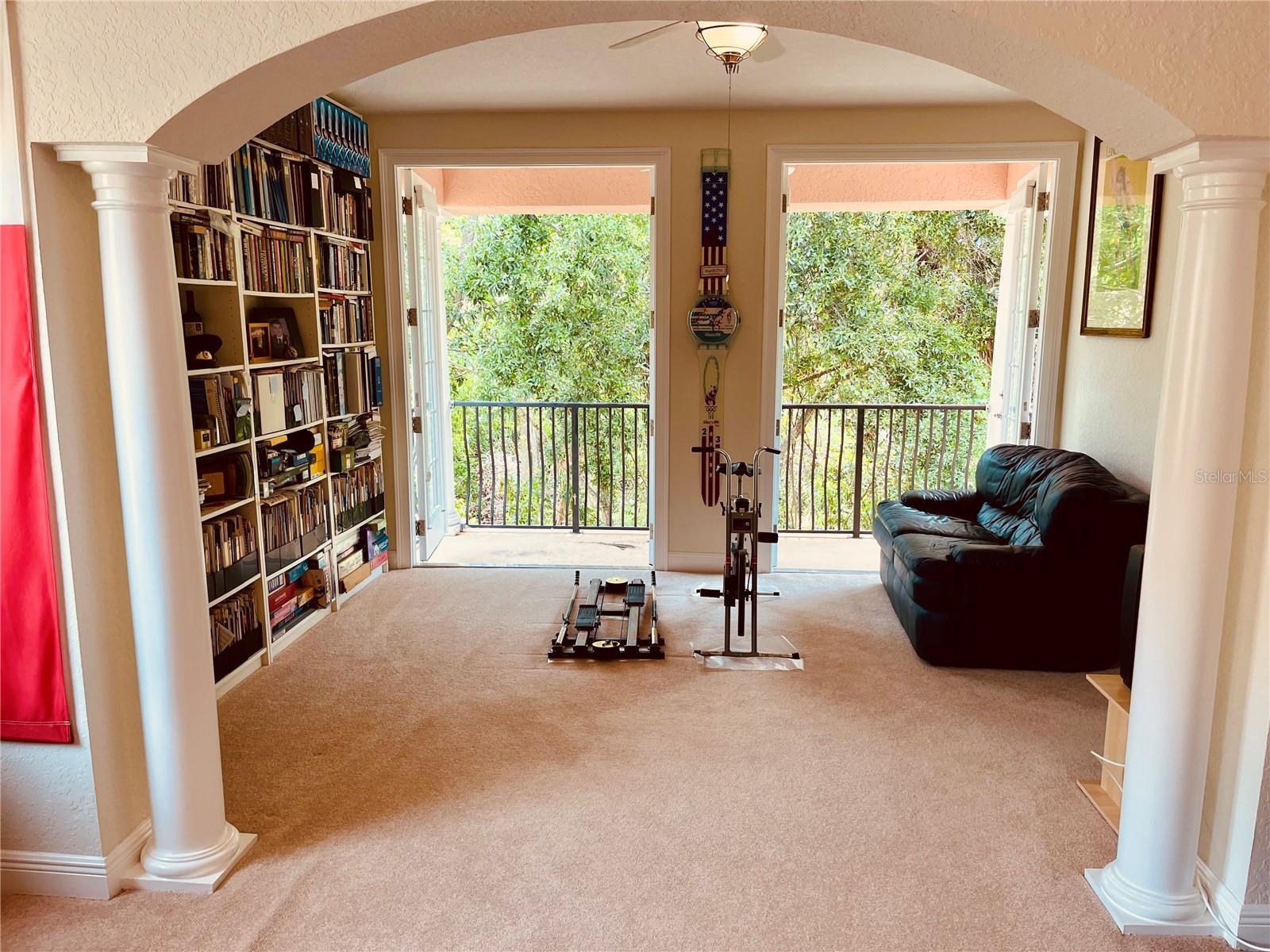 Primary bedroom through the pillars to the second bonus room and out the double French doors to the private back balcony