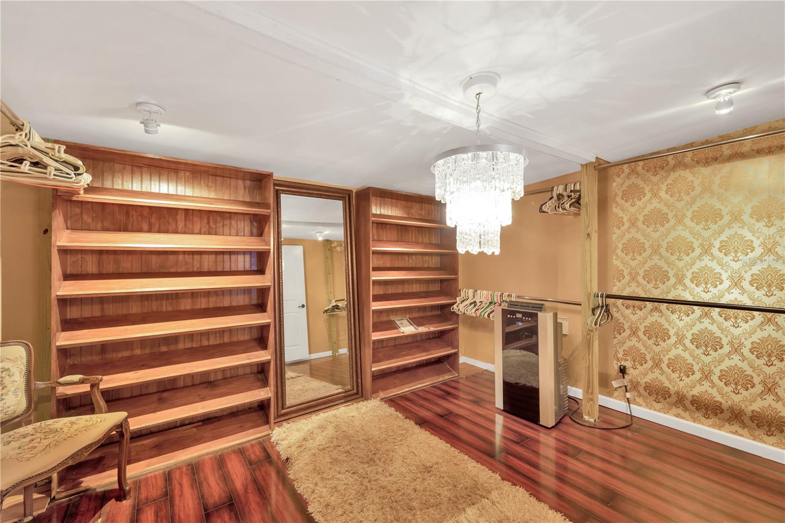 Impressive 12' x 14' walk-in closet off of the primary suite with built in shelving and an elegant chandelier.
