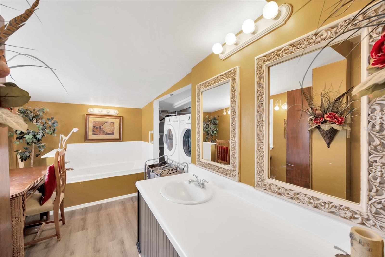 The en-suite bathroom features a jacuzzi tub with hand shower, a generous vanity with ample storage, and a closet concealing a full-sized washer and dryer.