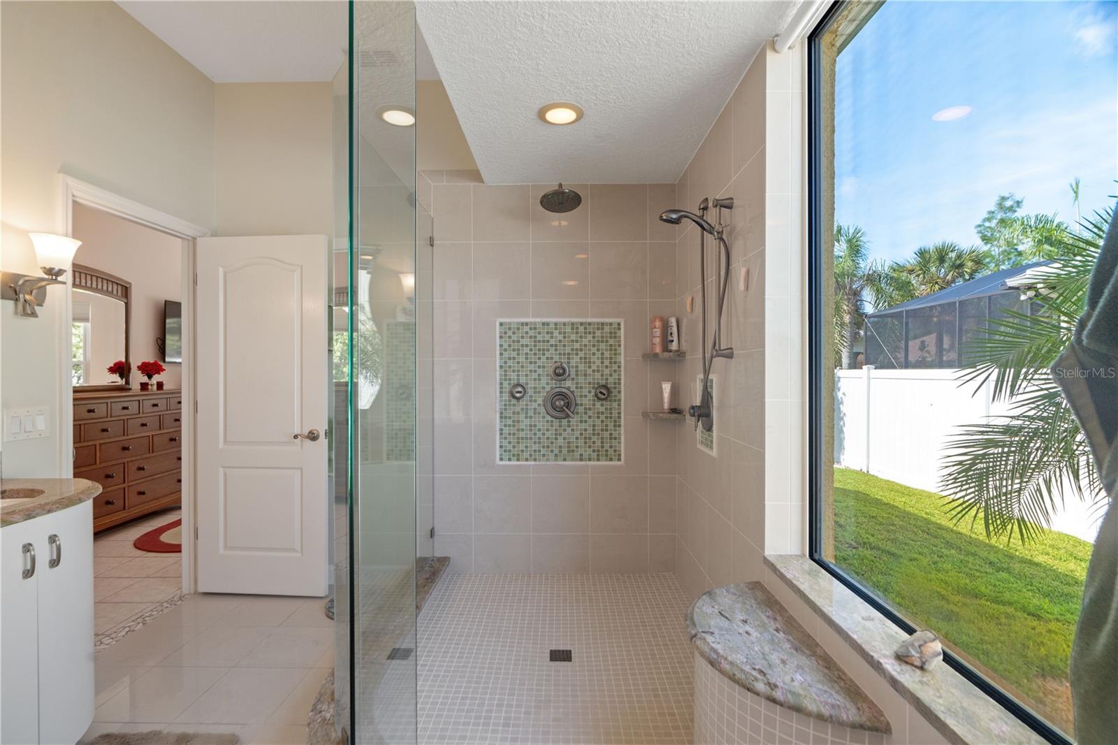 This shower is extra large and has multiple shower heads. Granite and tile accent seat in shower by the picture window.