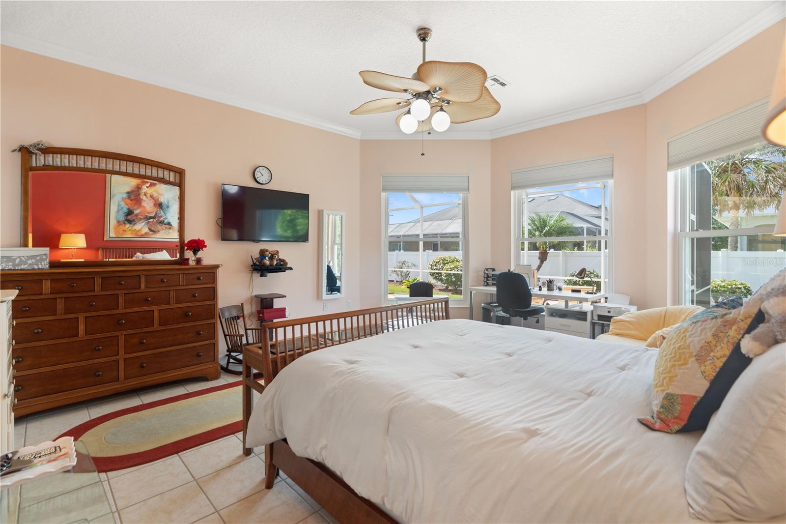 Crown molding adorns the ceiling. Behind the dresser and mirror is a french door that leads to the lanai.