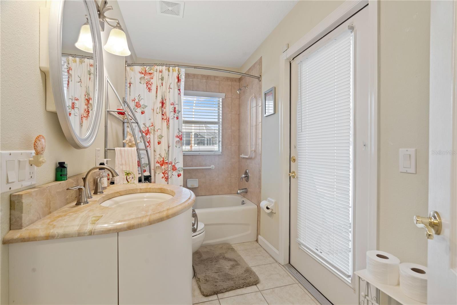 Second guest bathroom has a tub with shower and wall to wall tiles. French door leads to lanai.