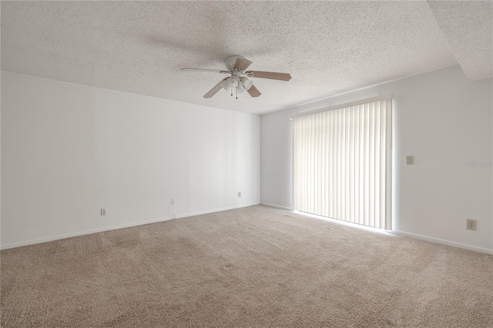 The Primary bedroom features carpet, neutral color palette a ceiling fan with light kit and sliding glass doors.