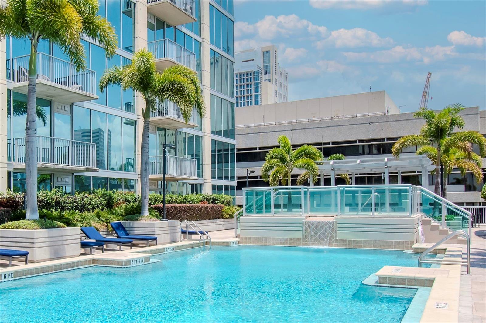 Upscale outdoor pool area with lounge seating, waterfall feature, and lush tropical landscaping.