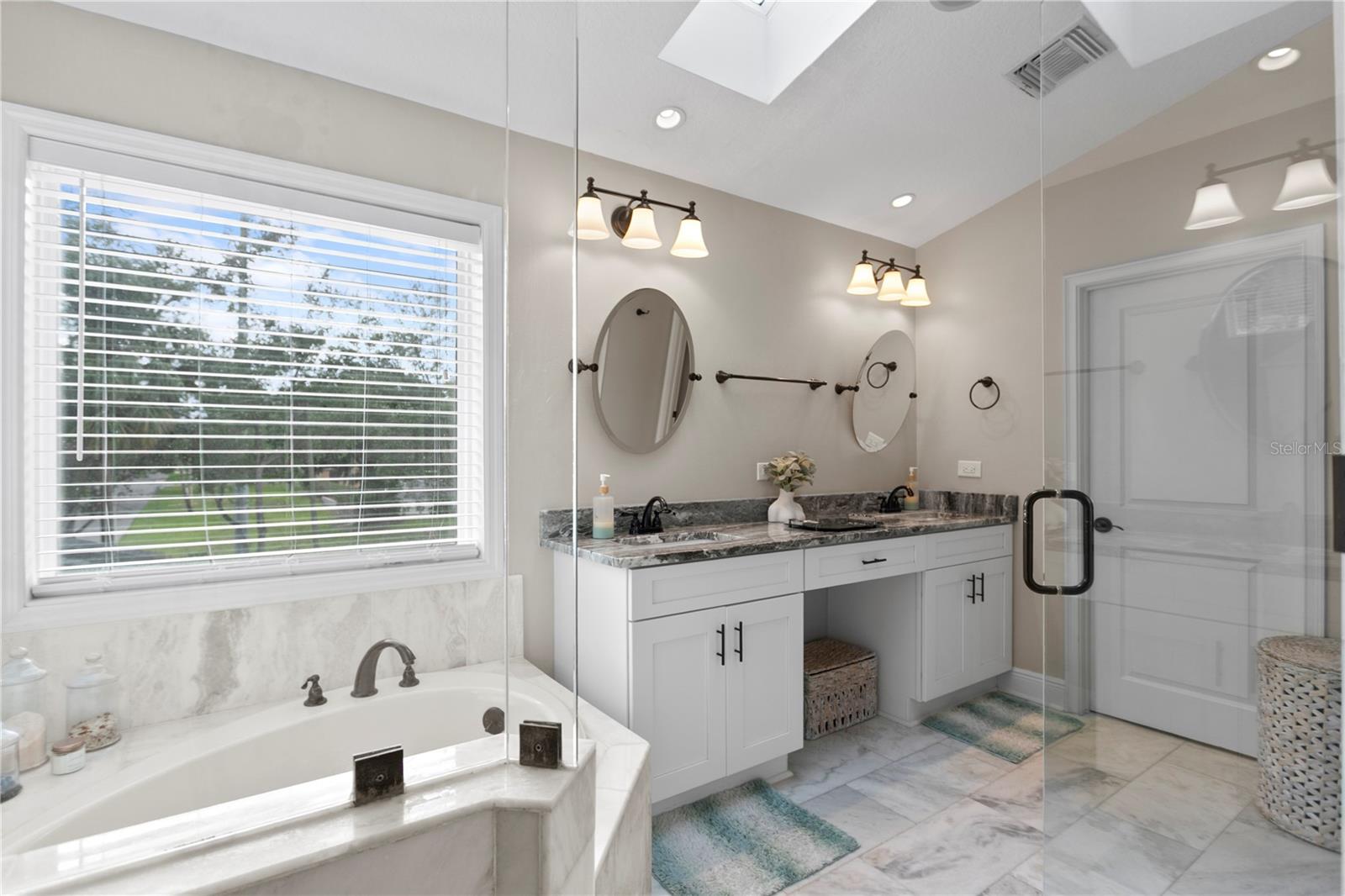Primary bathroom features a skylight, dual vanities and private water closet