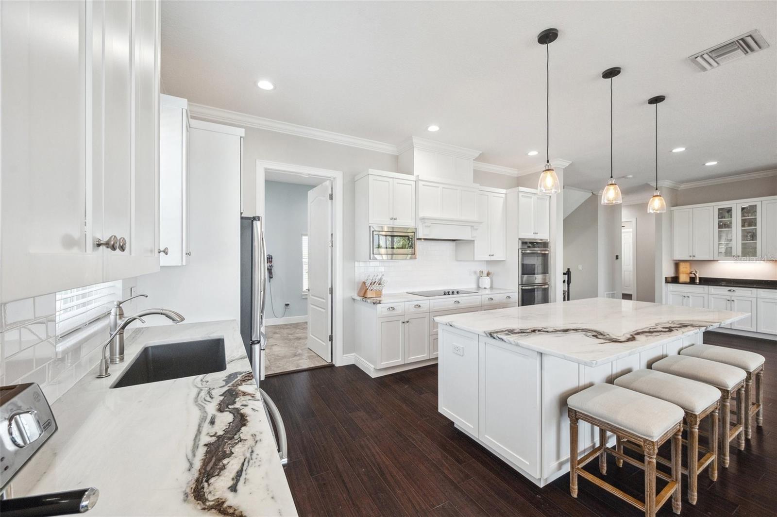 View of kitchen. The oversized island provides ample bar seating. Pantry/laundry room to back left.