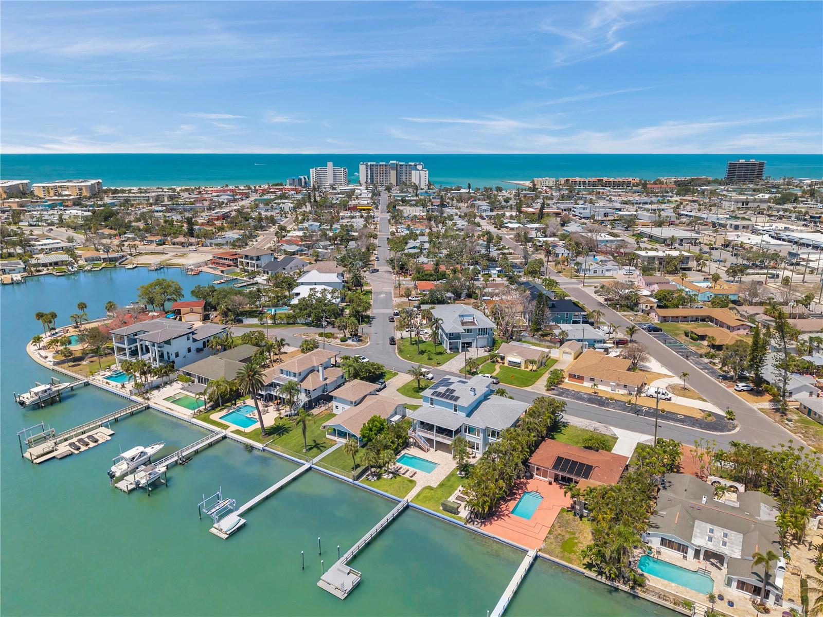 Aerial view showcasing the neighborhood of this luxury waterfront home, and the blue waters of the beach in the background.