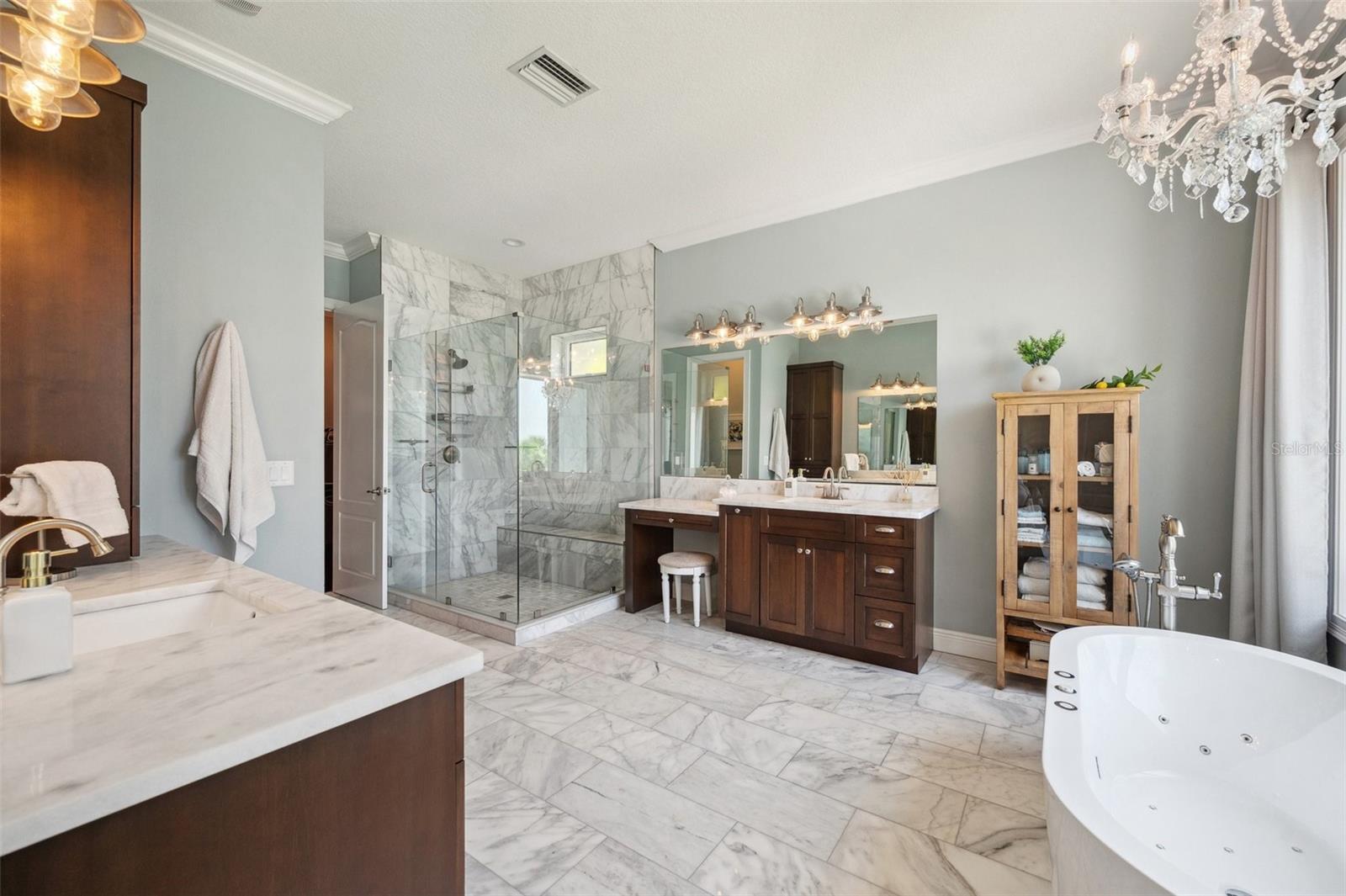 Luxurious master bathroom surrounded by real marble, jetted self-standing tub and his and her vanities. An oversized shower with bench seat completes this spacious and airy spa-like retreat! (also with wide open water view to the right from tub).