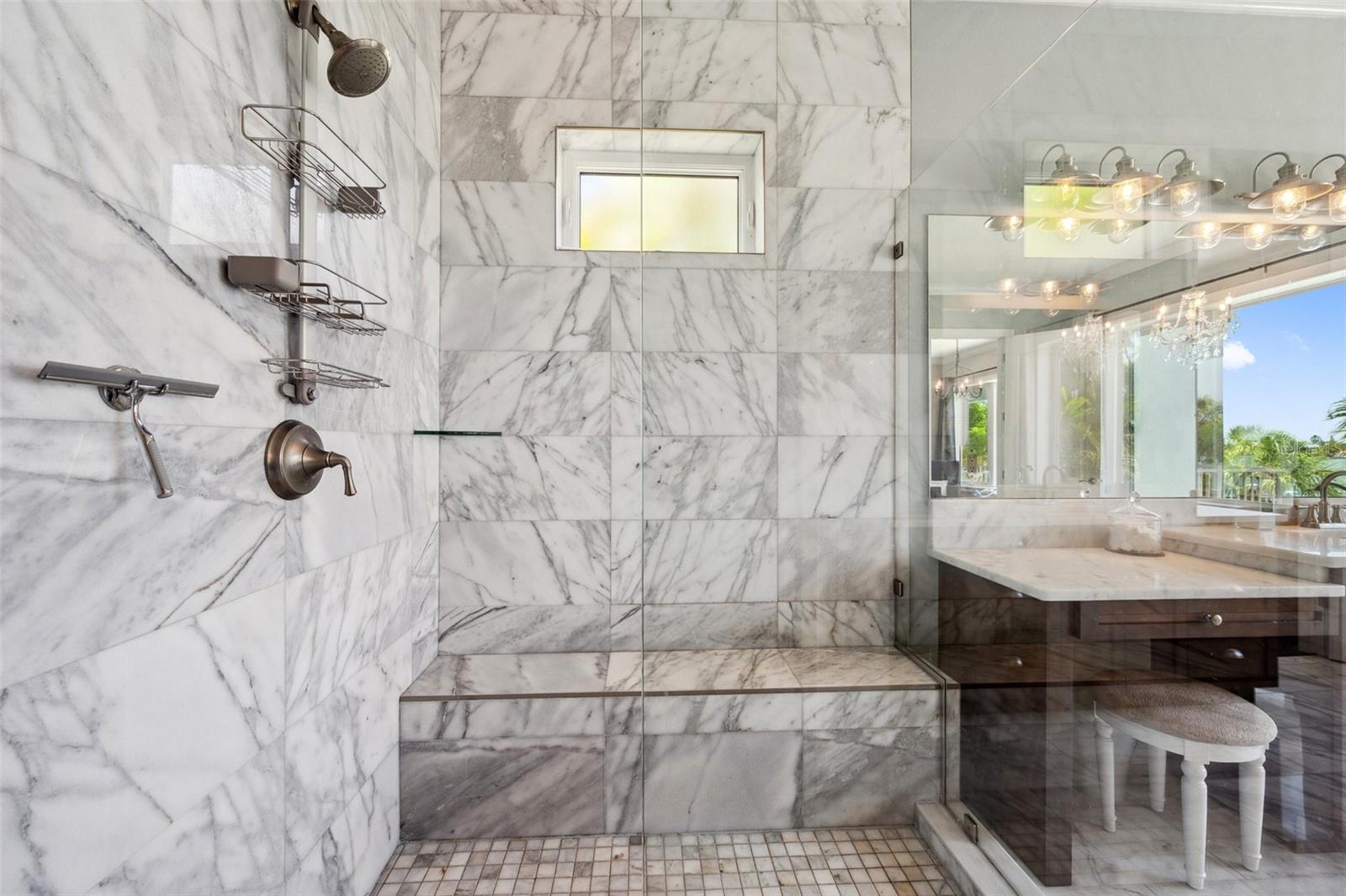 Oversized walk-in master shower with bench seat and real marble tile.
