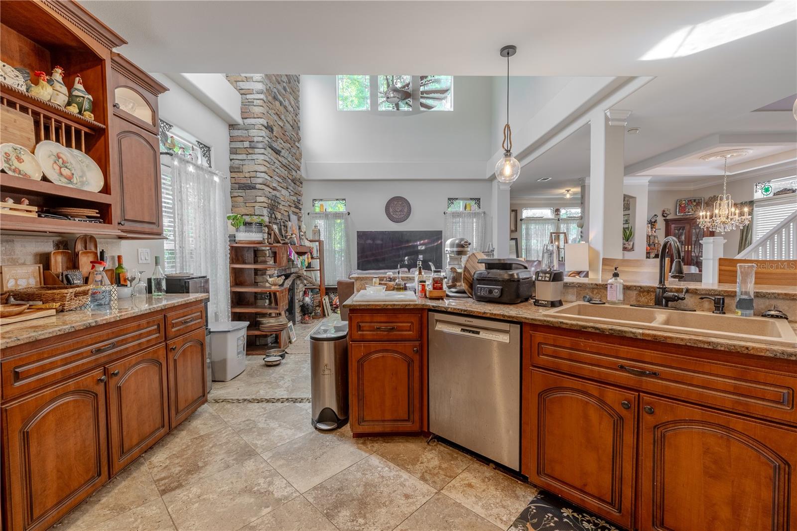 This well-appointed kitchen is the perfect blend of classic style and everyday functionality.Rich wood cabinetry with crown molding and glass-front accents provides generous storage, while granite countertops and a coordinating tile backsplash add timeless elegance. A custom arched range hood creates a stunning focal point above the stainless steel oven, complemented by matching appliances including a French door refrigerator and dishwasher. The open layout flows effortlessly into the living area, making it easy to entertain while cooking. Additional features include a deep dual-basin sink, built-in microwave niche, under-cabinet lighting, pendant accents, and abundant prep space for the home chef.