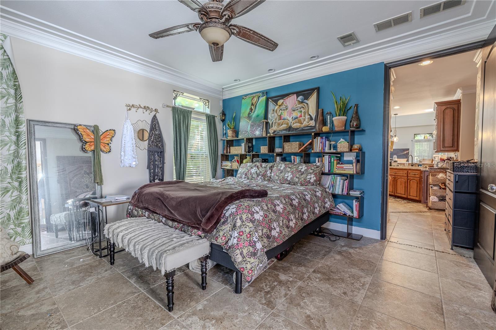 he spacious first-floor primary suite offers a peaceful retreat with direct access to the backyard oasis.?This light-filled room features crown molding, a designer ceiling fan, and large windows topped with decorative transoms that invite in natural light while maintaining privacy. Sliding glass doors lead directly to the patio, creating a seamless indoor-outdoor connection. The suite includes a generous walk-in closet and a private ensuite bath, offering comfort, convenience, and privacy—all just steps from the heart of the home.