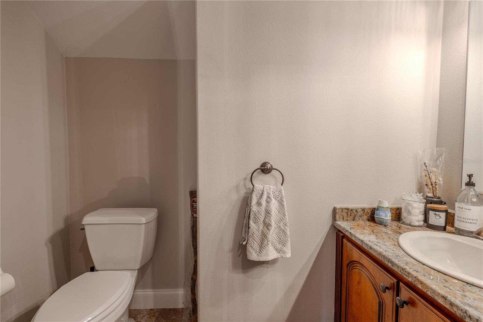 Conveniently located on the main level, the half bath offers classic comfort and style with a granite-topped vanity, under-mount sink, and rich wood cabinetry.Tucked beneath the staircase for smart use of space, this powder room is ideal for guests and everyday convenience. Neutral tones, quality finishes, and a thoughtful layout make it both functional and inviting.