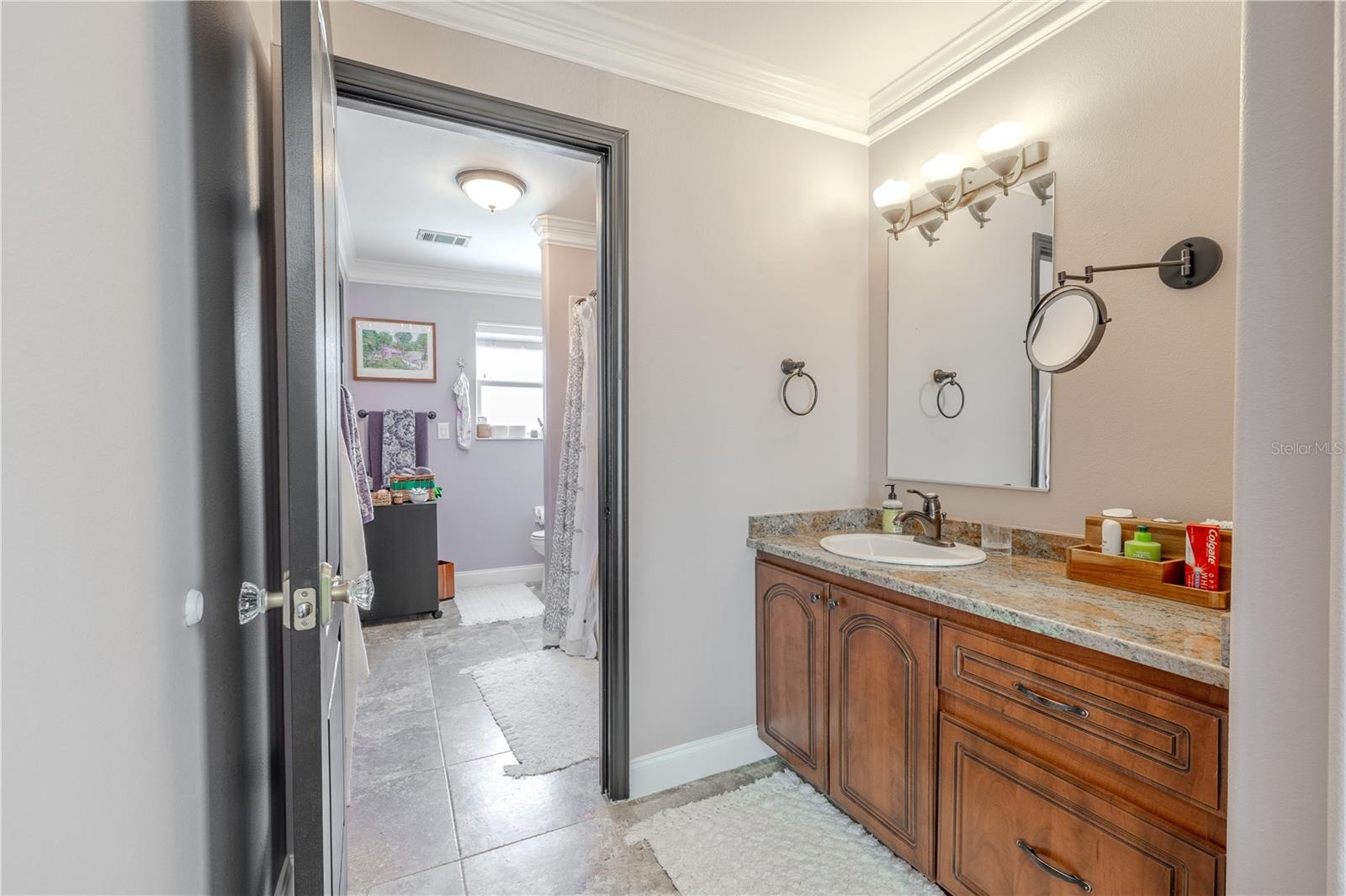This thoughtfully designed upstairs Jack and Jill bathroom offers convenience and privacy with dual access from adjoining bedrooms.The space features a granite-topped vanity with rich wood cabinetry, dual mirrors, and elegant lighting. A separate water closet and shower/tub combination provide practical functionality, making it ideal for sharing. Neutral tilework and crown molding add a polished touch, while the layout ensures everyone has room to get ready in comfort and style.