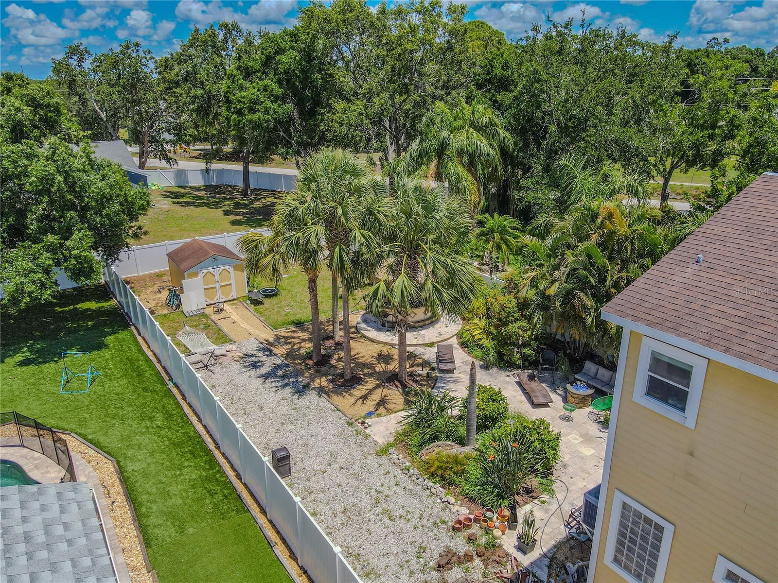 Escape to your private tropical retreat! This fully fenced backyard features mature palms, lush landscaping, a tiki-style outdoor bar and grilling area, a paver patio with lounge seating, a hammock zone, and a detached storage shed. Ideal for entertaining or relaxing in your own slice of paradise.