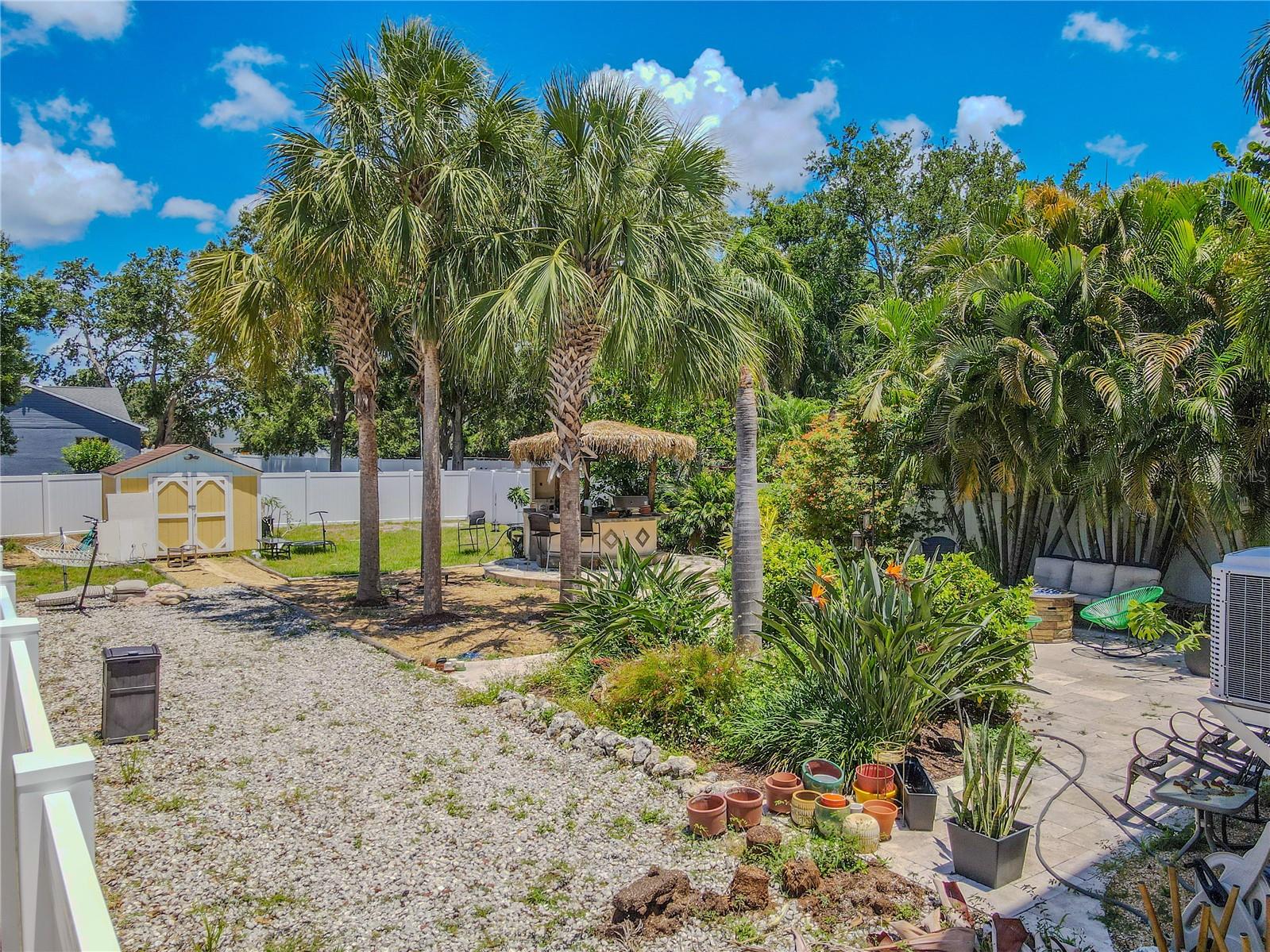 Escape to your private tropical retreat! This fully fenced backyard features mature palms, lush landscaping, a tiki-style outdoor bar and grilling area, a paver patio with lounge seating, a hammock zone, and a detached storage shed. Ideal for entertaining or relaxing in your own slice of paradise.