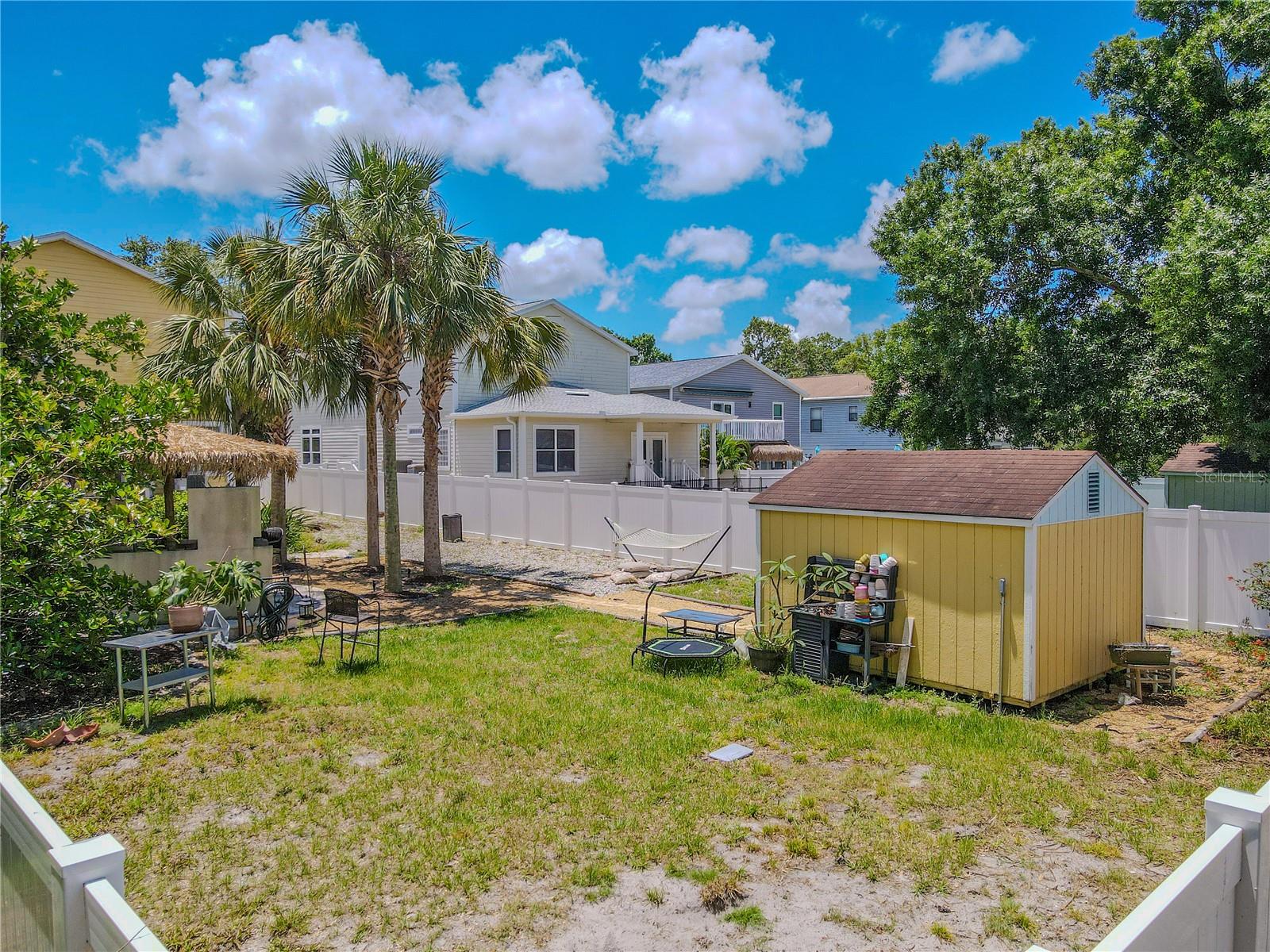 Escape to your private tropical retreat! This fully fenced backyard features mature palms, lush landscaping, a tiki-style outdoor bar and grilling area, a paver patio with lounge seating, a hammock zone, and a detached storage shed. Ideal for entertaining or relaxing in your own slice of paradise.