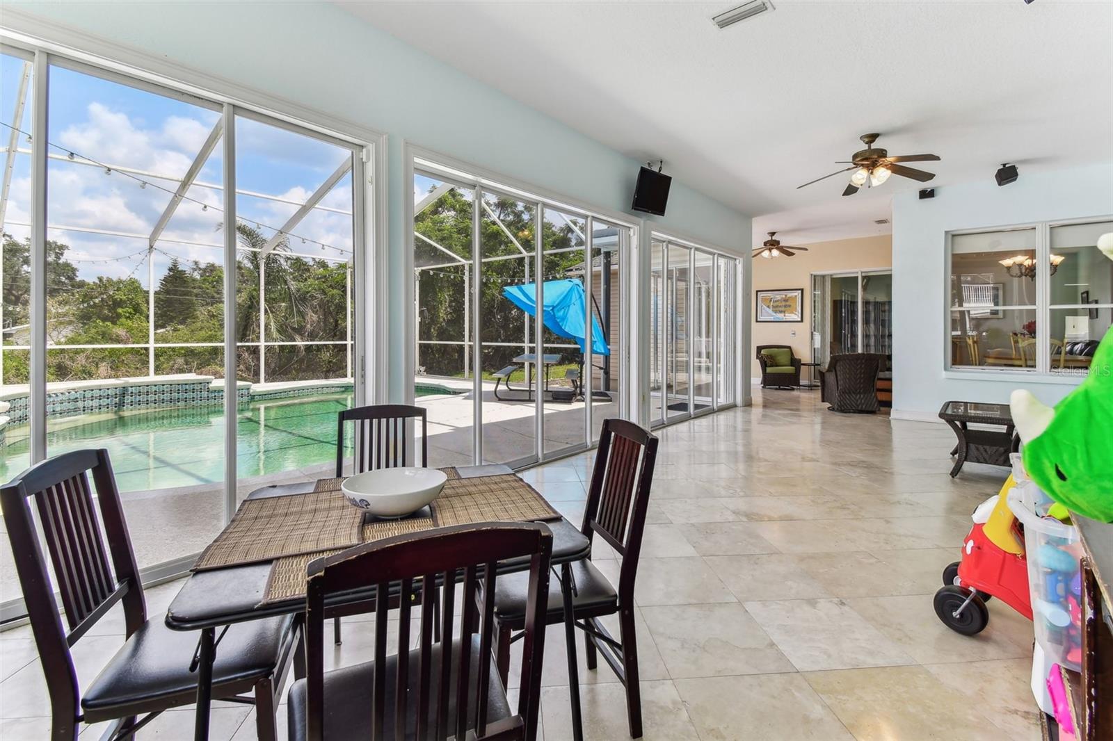 Bright Florida room with travertine flooring and panoramic windows overlooking the pool and backyard — perfect for relaxing year-round.
