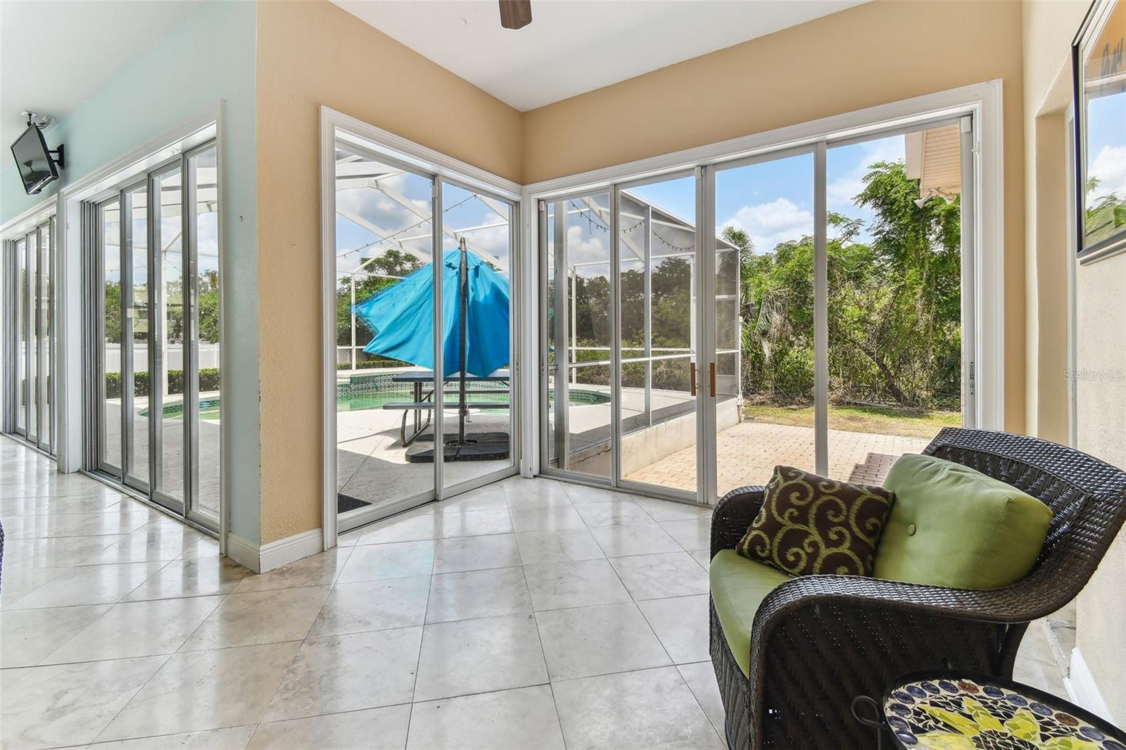 Bright Florida room with travertine flooring and panoramic windows overlooking the pool and backyard — perfect for relaxing year-round.