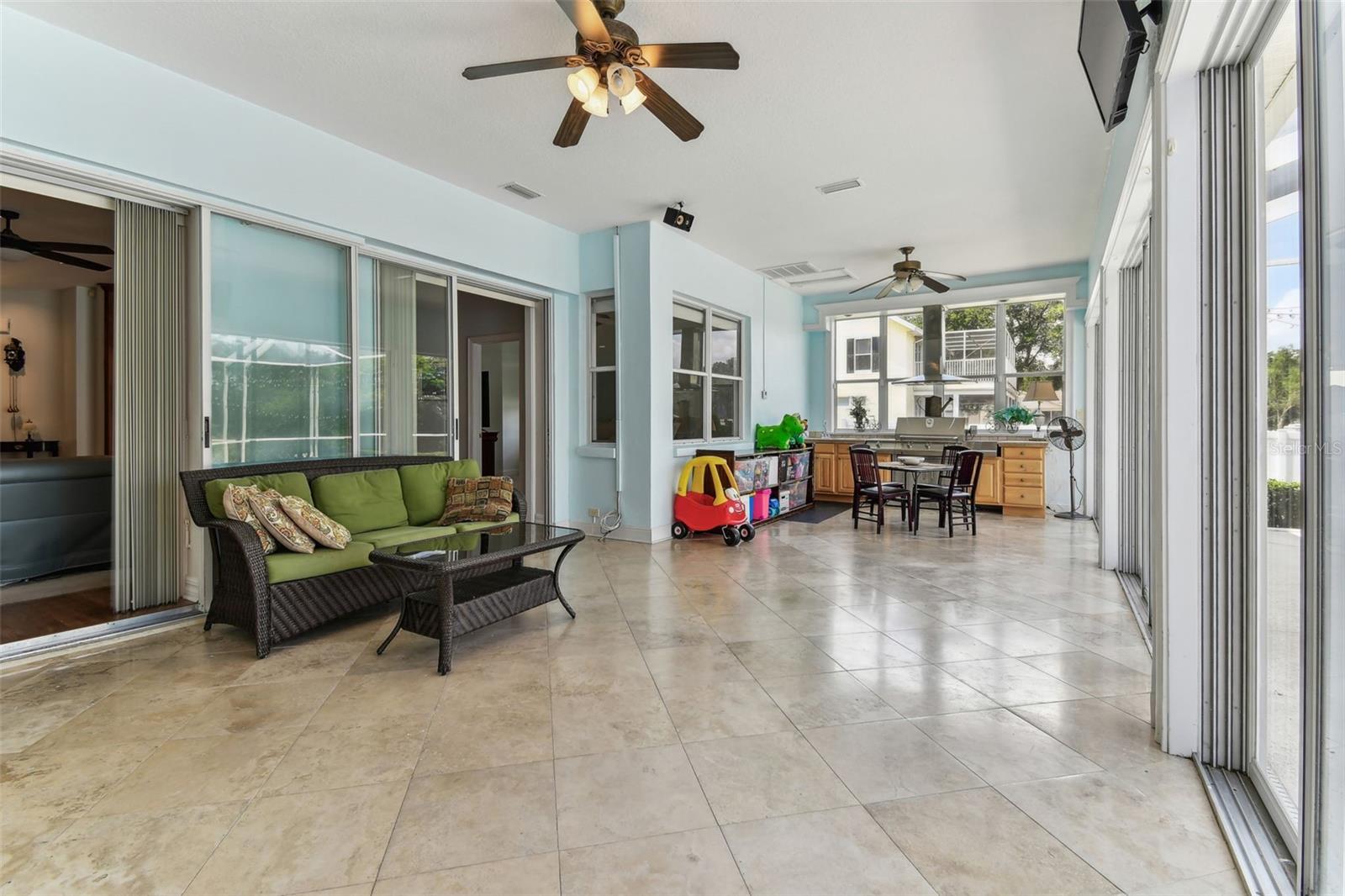 Bright Florida room with travertine flooring and panoramic windows overlooking the pool and backyard — perfect for relaxing year-round.