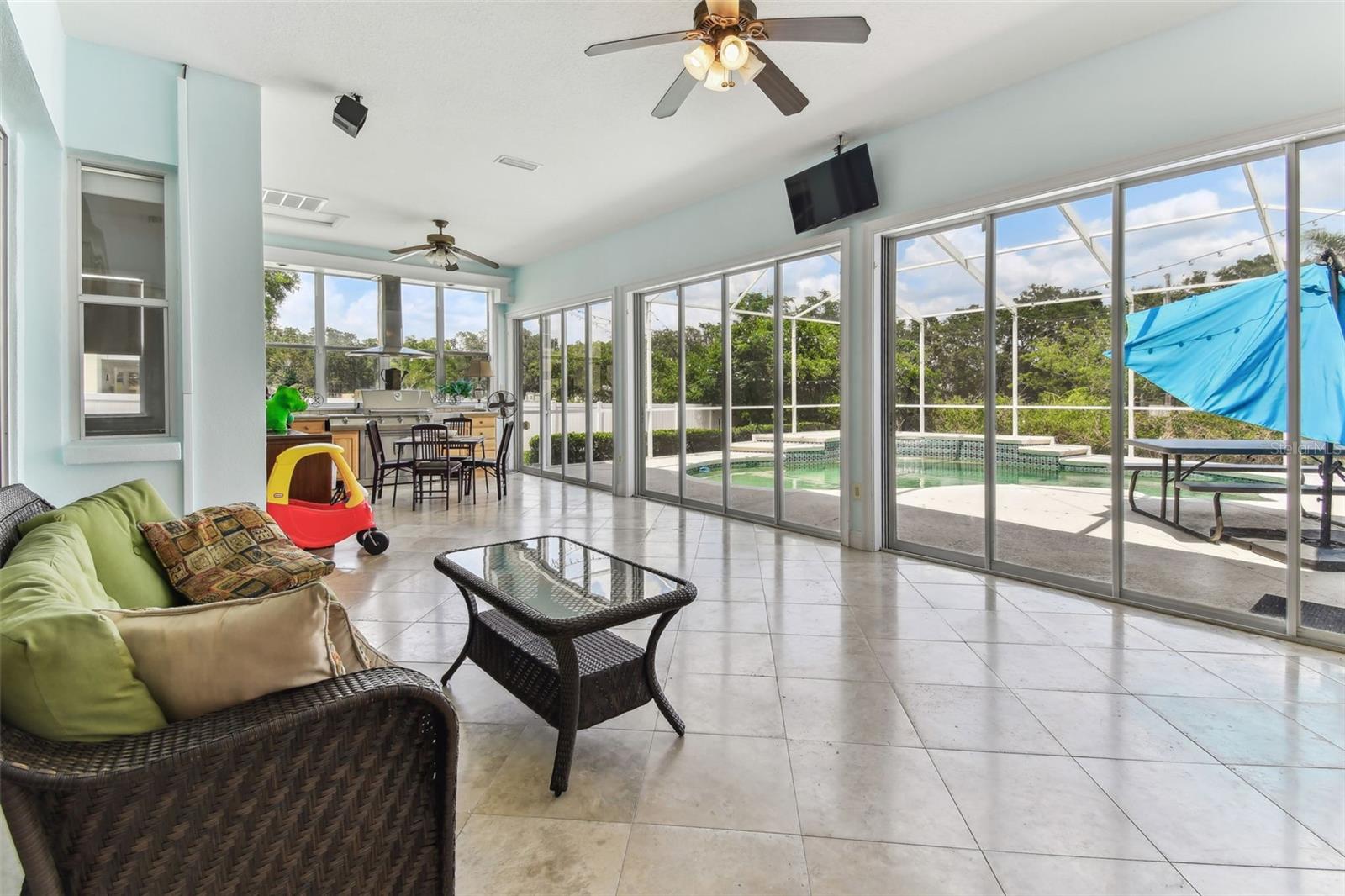 Bright Florida room with travertine flooring and panoramic windows overlooking the pool and backyard — perfect for relaxing year-round.