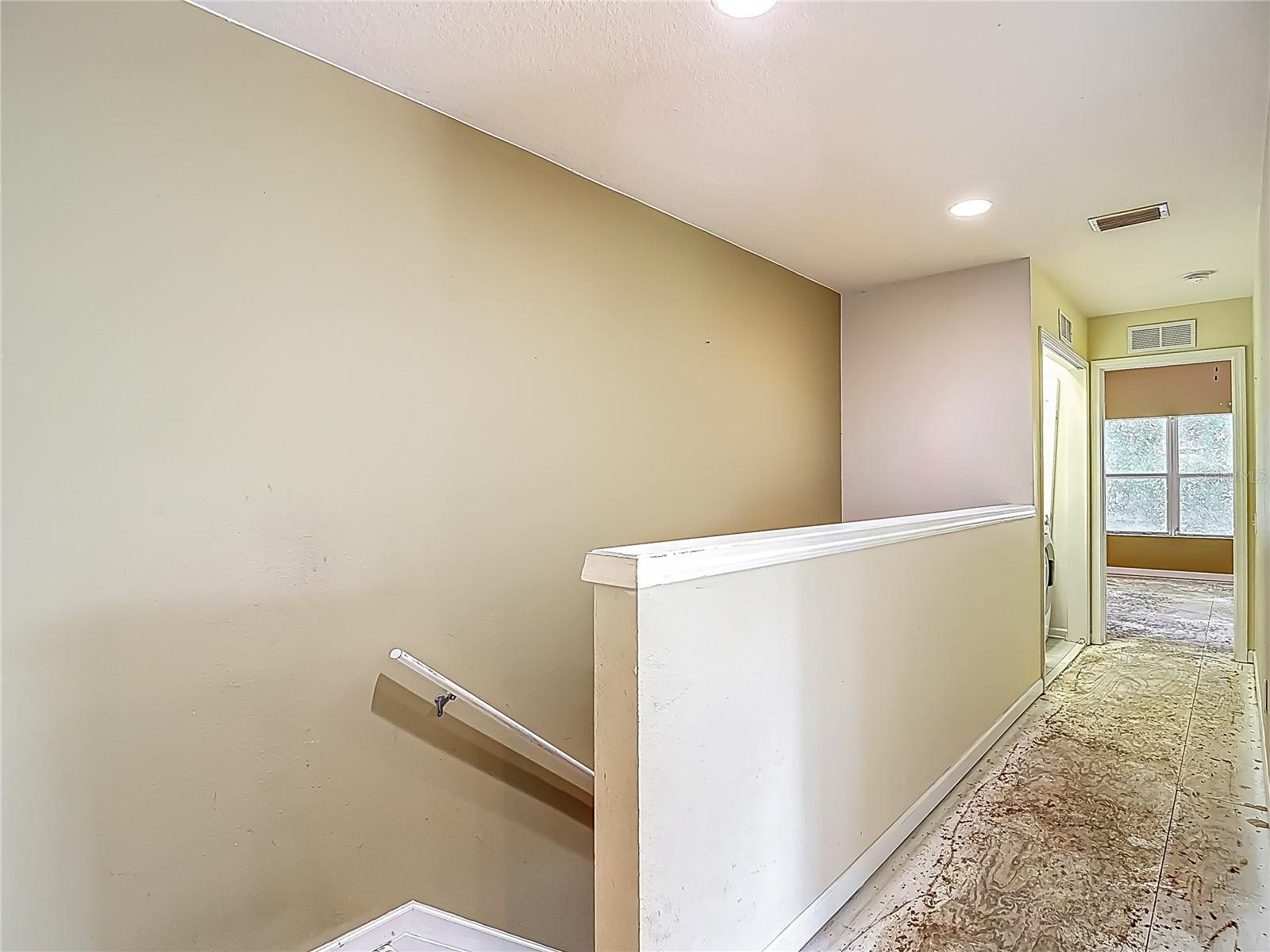 At the top of the stairs. Behind you is bedroom 1(grey wall) That bedroom faces the front of the townhome and is above the garage. Down this hall: bedroom 2, laundry closet then primary bedroom, overlooking the trees & pond and features en suite bath.
