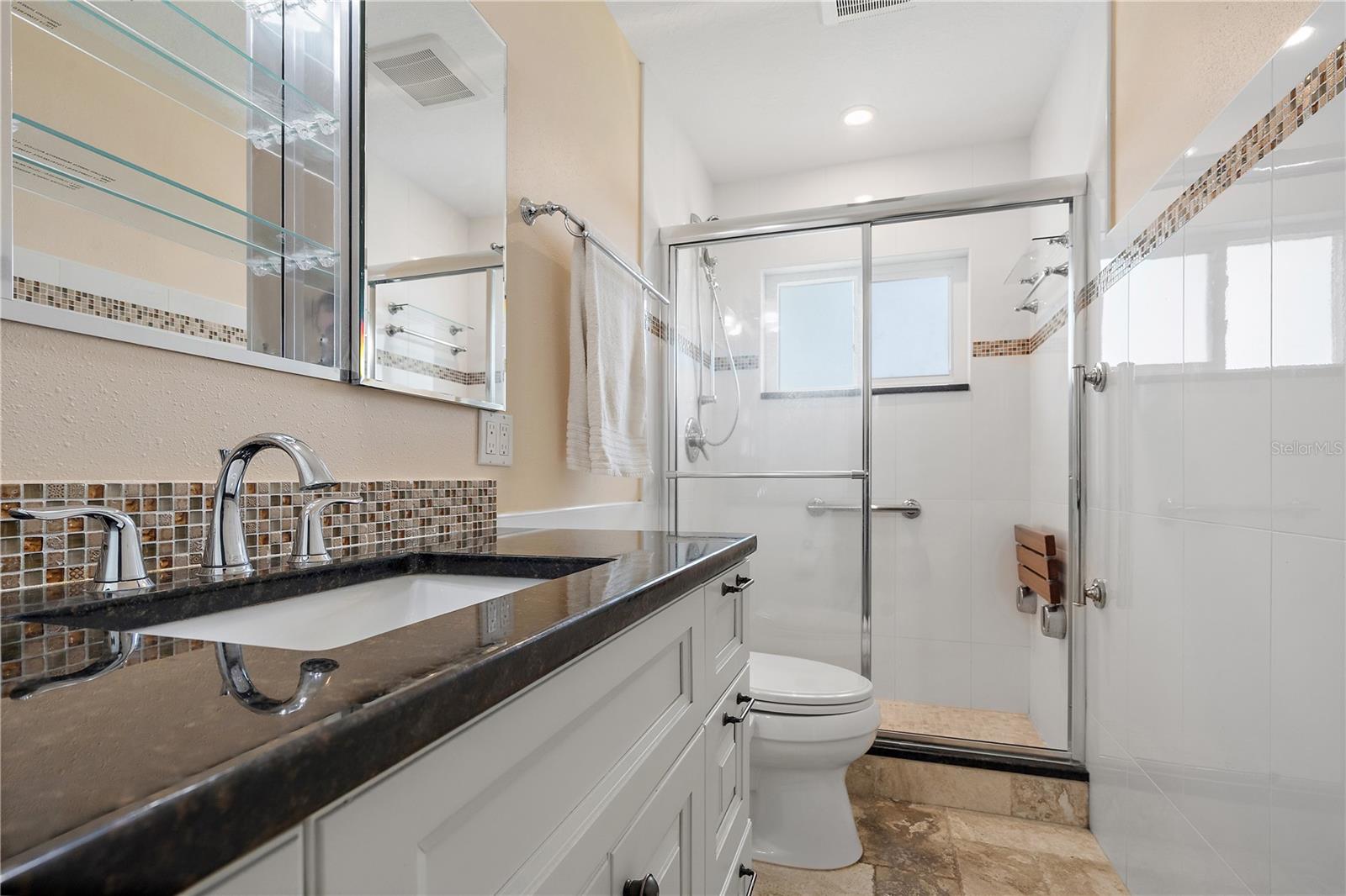 En suite primary bath with granite vanity top and shower seat