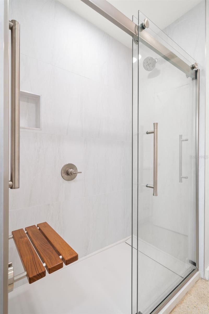 Walk in shower, teak bench complimented by luxury glass doors.