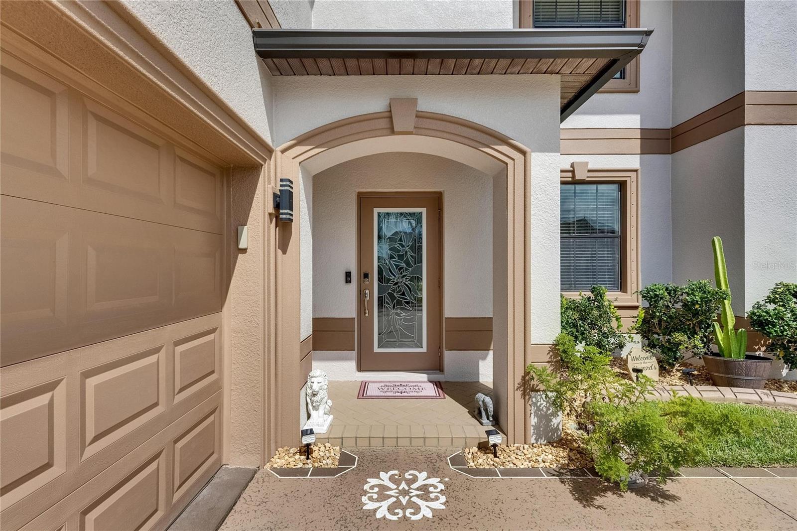 An elegant front entry showcases detailed concrete artistry and brick edging, beautifully complementing the meticulously maintained landscaping.
