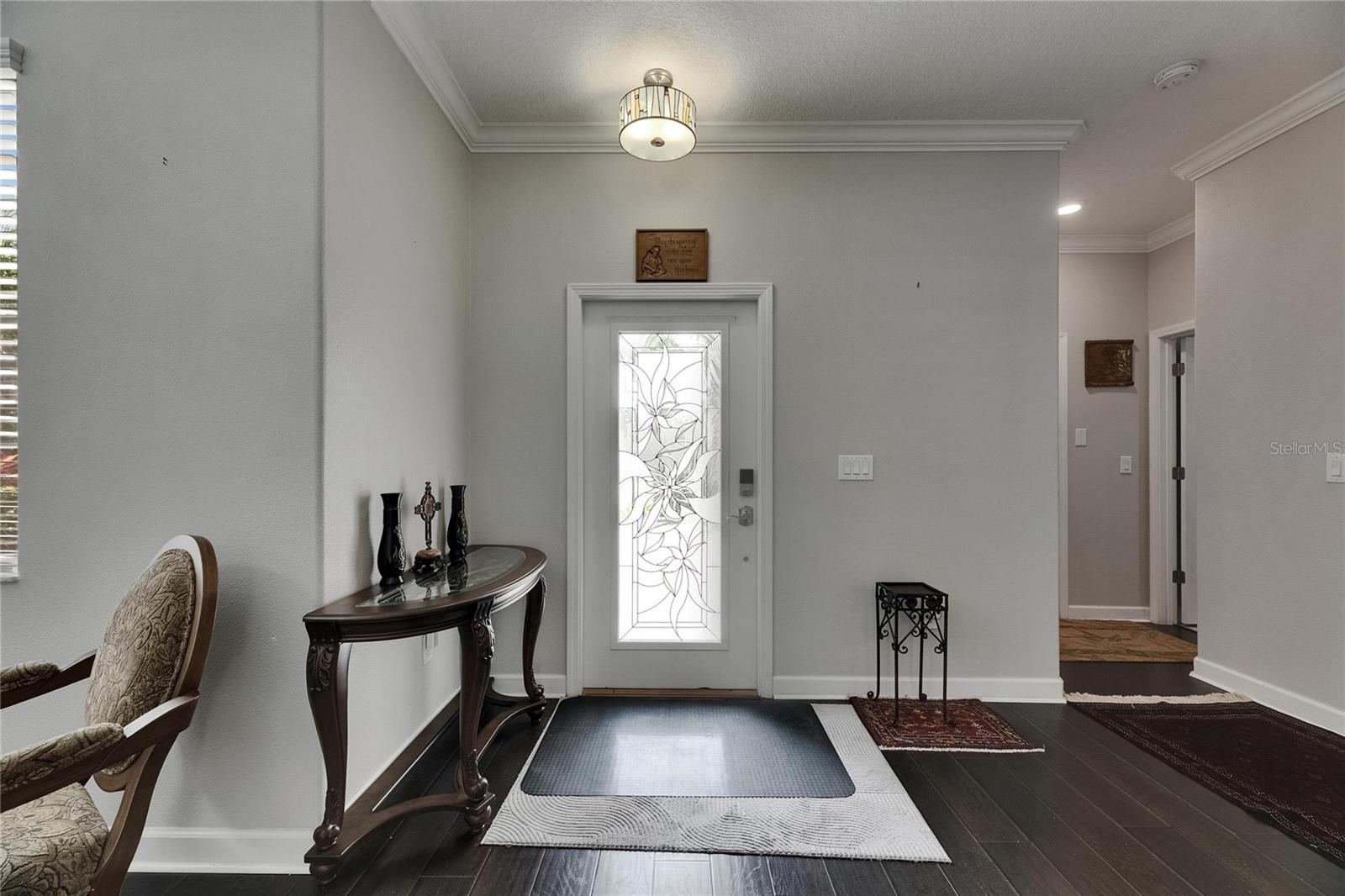 An impressive glass front door opens to a grand two-story foyer featuring rich wood floors and a striking front entry chandelier.