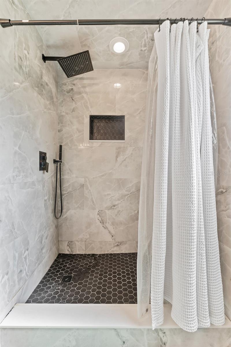 Step into luxury with this oversized walk-in shower, featuring floor-to-ceiling tile, black hex floor, and a rain-style showerhead—designed for ultimate relaxation.