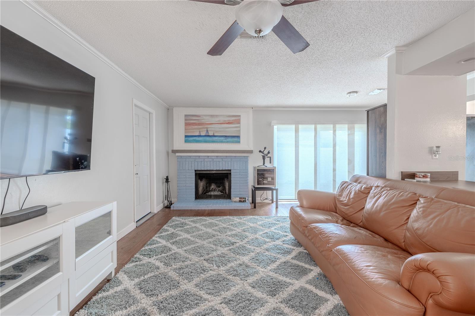 Comfort meets functionality in this inviting family room. The open layout ideal for both everyday living and entertaining. A cozy wood-burning fireplace (chimney cap was replaced and the chimney cleaned and inspected in 2022) anchors the space, gives warmth and charm, while large windows and sliding doors fill the room with natural light and provide easy access to the backyard. The open connection to the kitchen and adjacent living areas enhances the flow of the home. With plenty of room for seating and media, this versatile space is perfect for movie nights, gatherings, or simply relaxing at the end of the day.