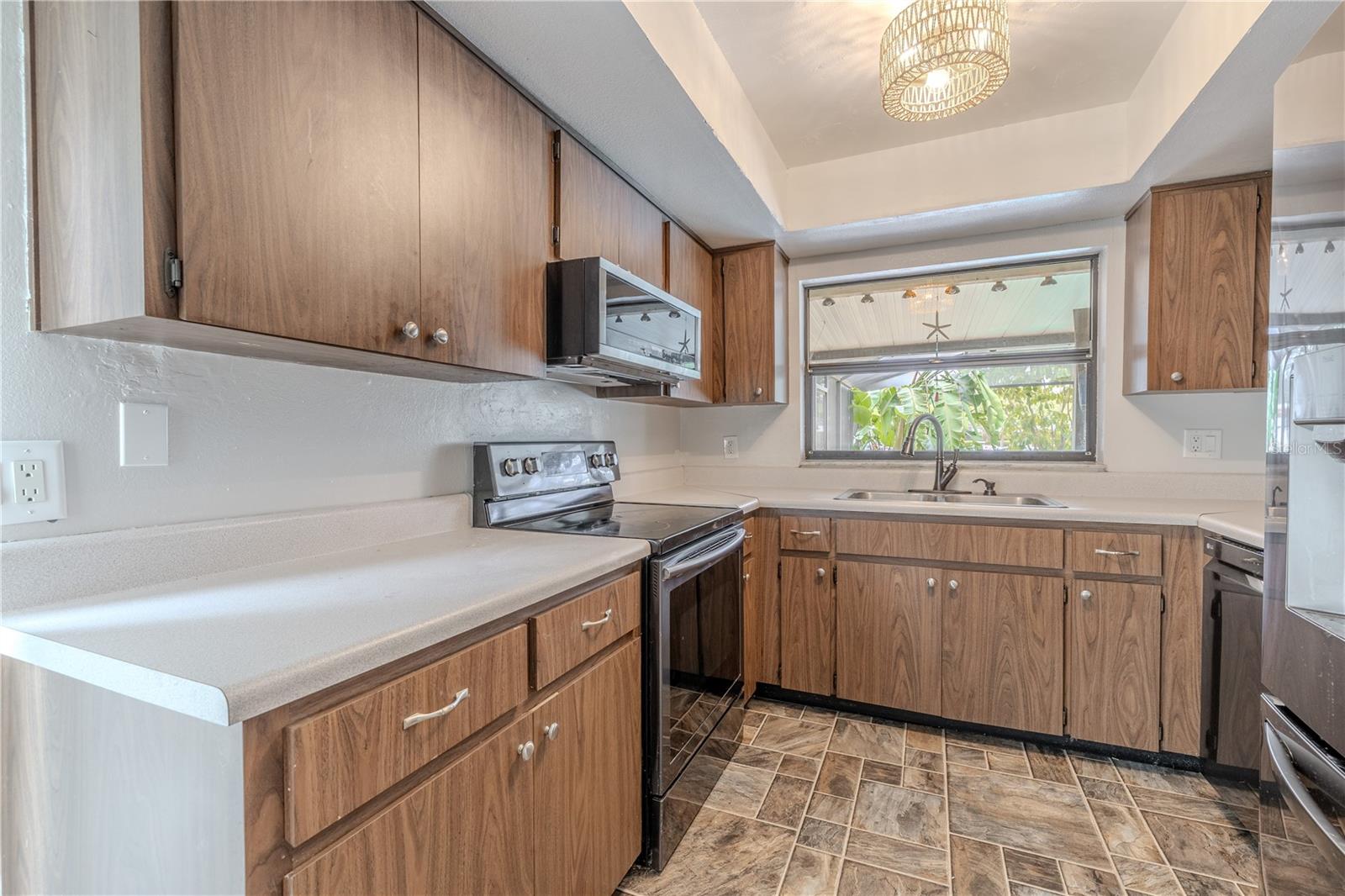 Durable cabinets feature a wood-look finish, complemented by solid surface countertops and a large window over the sink that brings in natural light and a view of the backyard.