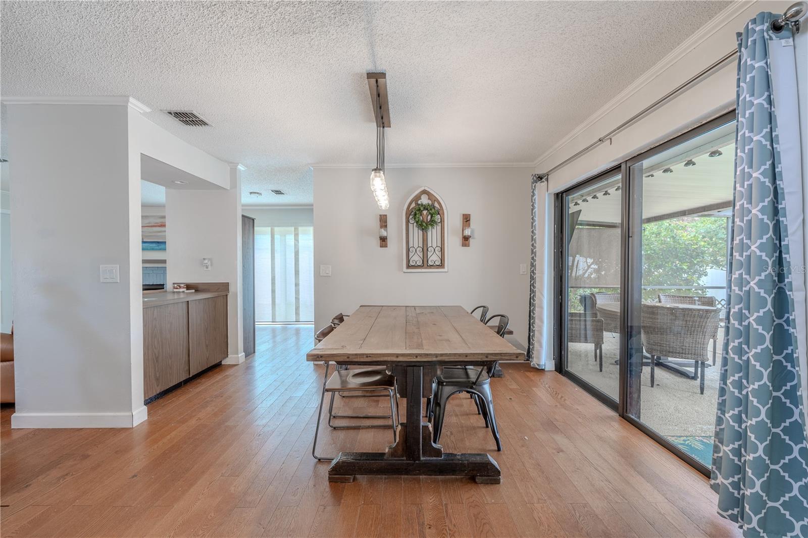 Spacious dining area with hardwood floors also has direct access to the screened lanai and pool through large sliding glass doors, creating a seamless indoor-outdoor flow. A modern light fixture adds character and illuminates the space, while the open sightlines to the living room and kitchen enhance the home’s open-concept feel. This inviting space comfortably accommodates a large dining table and provides a relaxed yet functional setting for gathering.