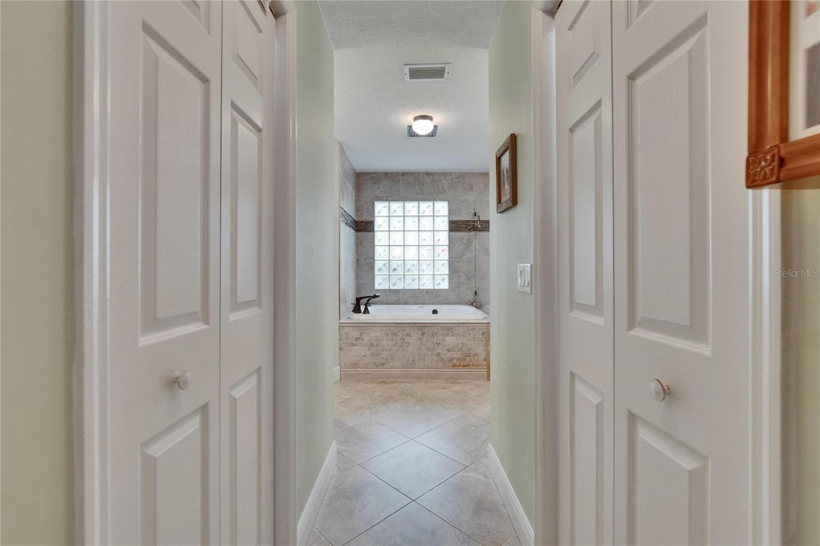 Primary Suite walk-in closets on both sides of hall and view to the tub.