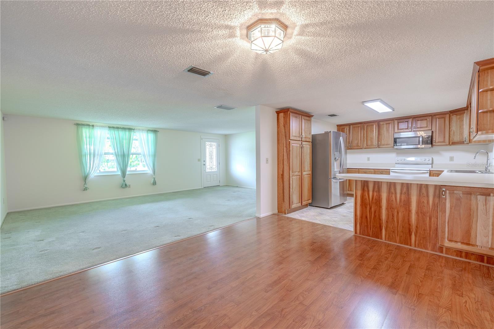 Just beyond the family room, the kitchen features warm wood cabinetry, a convenient breakfast bar, and direct access to additional living and dining areas—all easily visible from the heart of the home.
