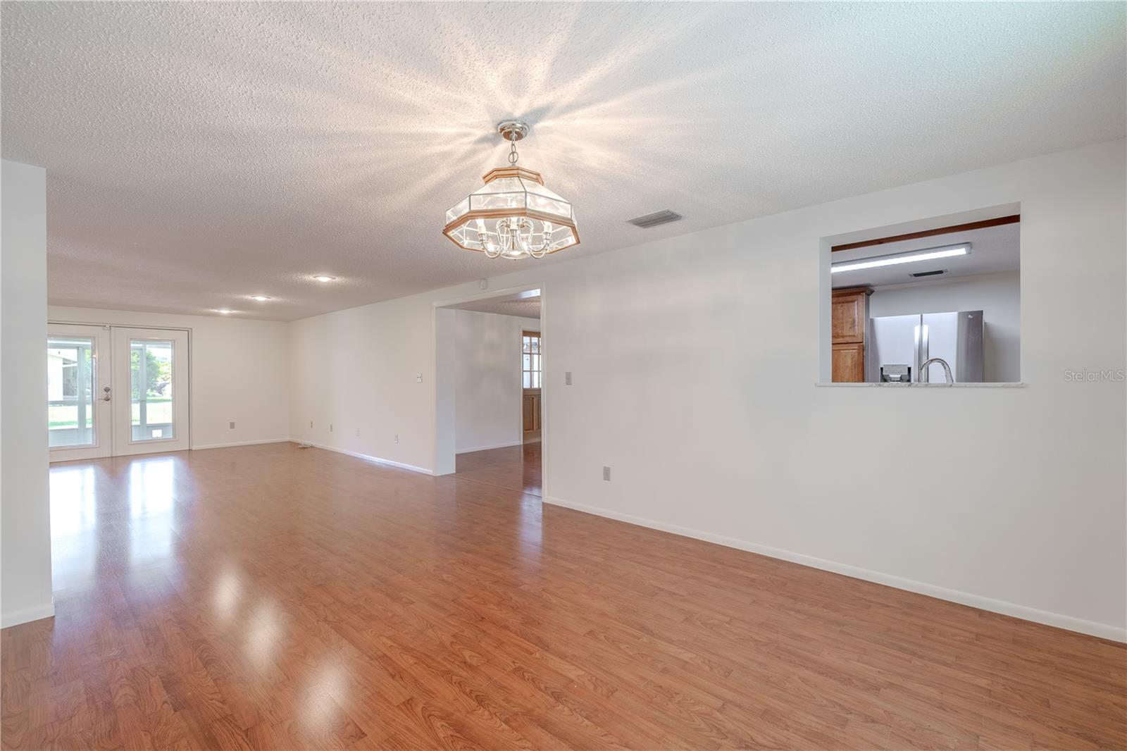 The dedicated dining area features warm laminate flooring that adds both durability and style, creating a seamless flow with the adjacent living spaces. A classic overhead light fixture anchors the space and offers a soft, inviting glow for evening meals. Generously sized, this room can easily accommodate a large dining table with room to spare. A passthrough to the kitchen adds convenience and connectivity, while nearby access to the backyard and other living areas makes this an ideal spot for everyday dining or hosting special gatherings.