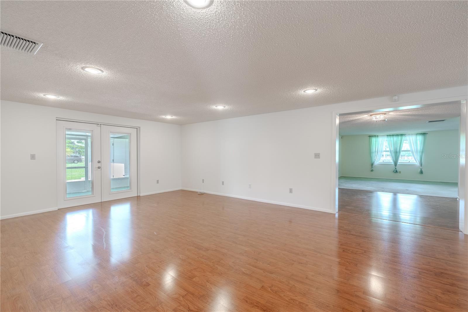 This expansive living room offers incredible flexibility with its open layout, neutral walls, and durable laminate flooring. Recessed lighting enhances the bright and airy atmosphere, while double glass doors provide direct access to the screen in porch and backyard and allowing natural light to flood the space.