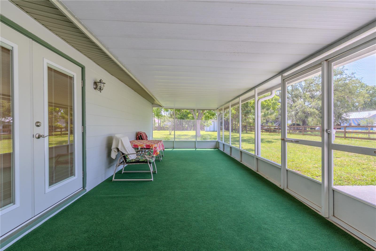 Enjoy the best of Florida living on this spacious screened-in back porch, perfect for relaxing or entertaining year-round. Fully enclosed with large screened panels, this outdoor retreat offers unobstructed views of the backyard while keeping pests at bay. A durable, low-maintenance green outdoor carpet adds comfort underfoot and defines the space with a pop of color. The covered roof provides shade and protection from the elements, making it ideal for morning coffee, evening dinners, or weekend gatherings. Accessible through a set of glass French doors, this porch extends your living space into the outdoors with ease and charm.
