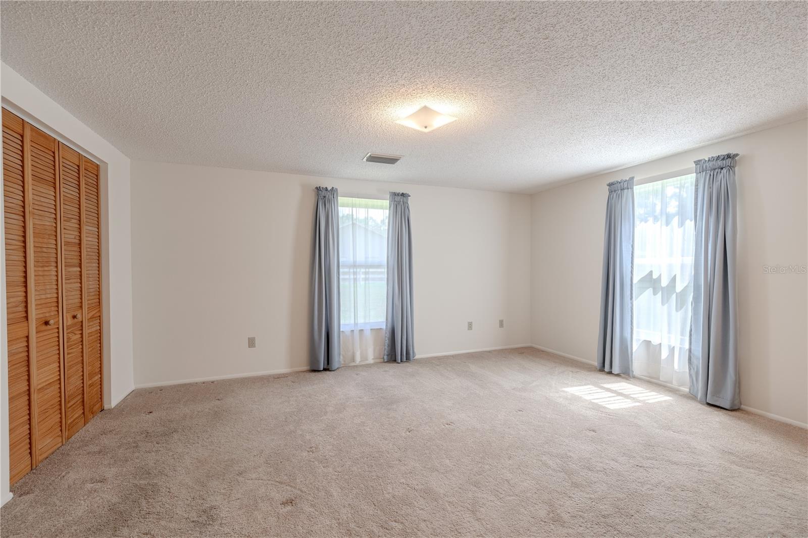 This spacious primary bedroom offers comfort, functionality, and an abundance of storage. With two large windows providing soft natural light and views of the backyard, the room feels open and inviting. Neutral walls and carpeting create a warm, relaxing atmosphere, ready to complement any personal style.