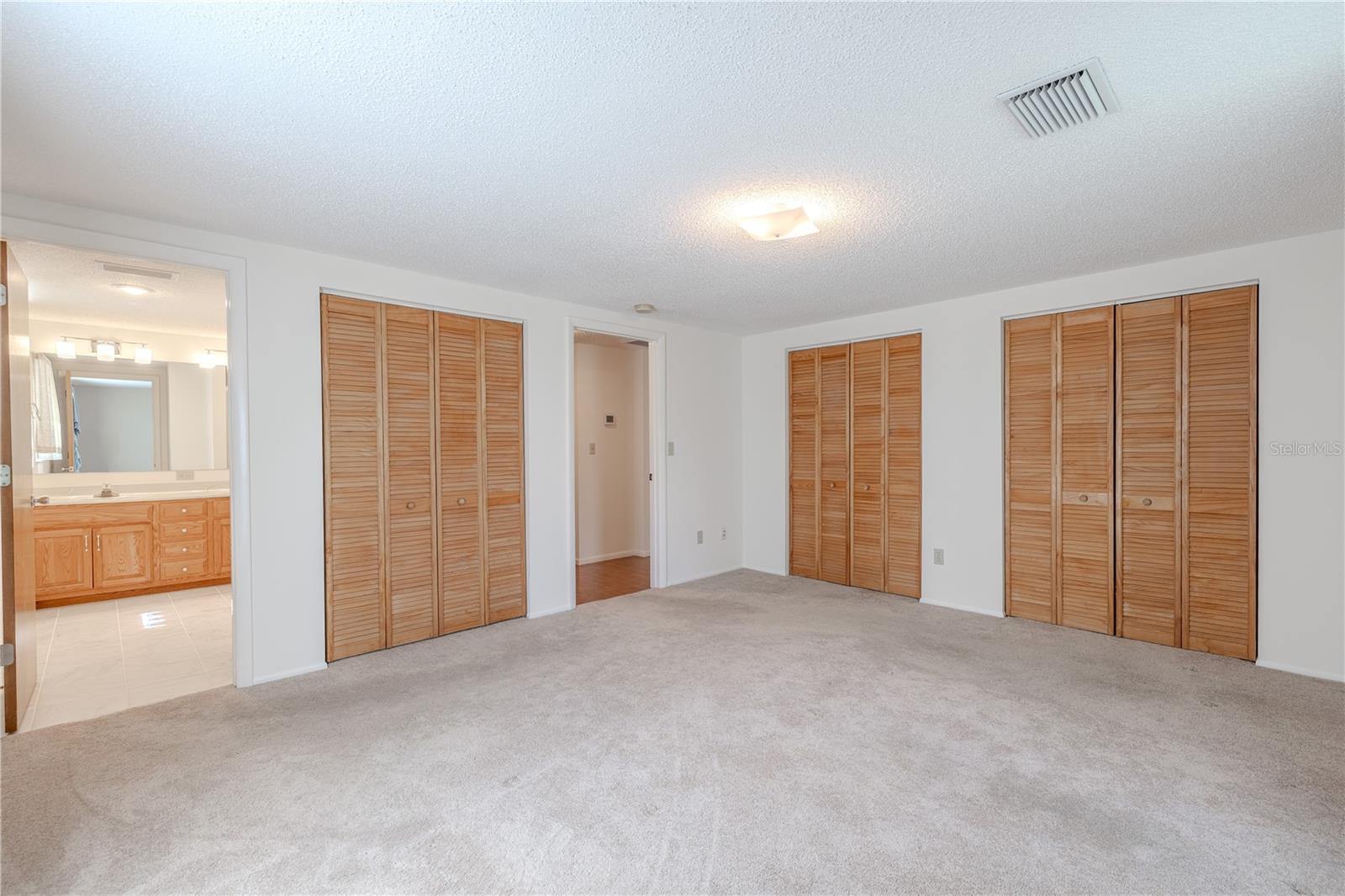 Multiple closets with louvered doors—including a double closet with built-in shelving—offer ample storage and easy organization. An ensuite bathroom is just steps away