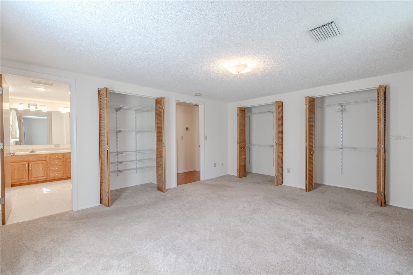Multiple closets with louvered doors—including a double closet with built-in shelving—offer ample storage and easy organization. An ensuite bathroom is just steps away
